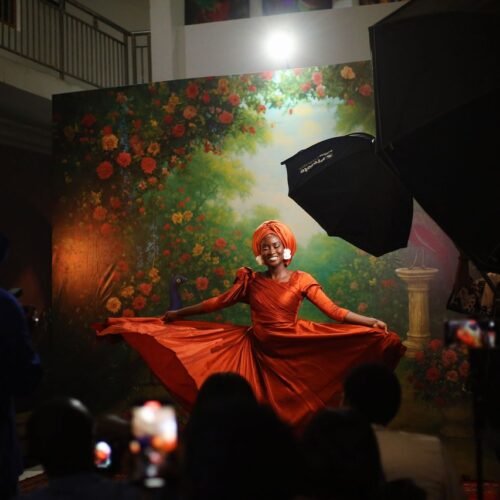 pexels-photo-35073805-35073805 A woman in an orange dress poses gracefully indoors with a vibrant floral backdrop in Abuja, Nigeria.